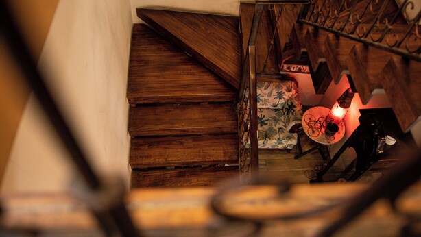 A wooden staircase with a metal railing, a table with a red light, and a floral-patterned wall. - Hotel SB Cuenca (Cuenca)