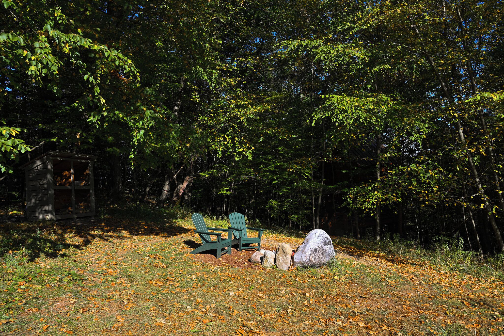 Een bebost gebied met twee Adirondack stoelen en een grote rots.