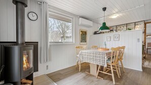 A cozy room with a wood-burning stove, a dining table with chairs, and a window with curtains. - Stunning home in Glesborg with WiFi (Glesborg)