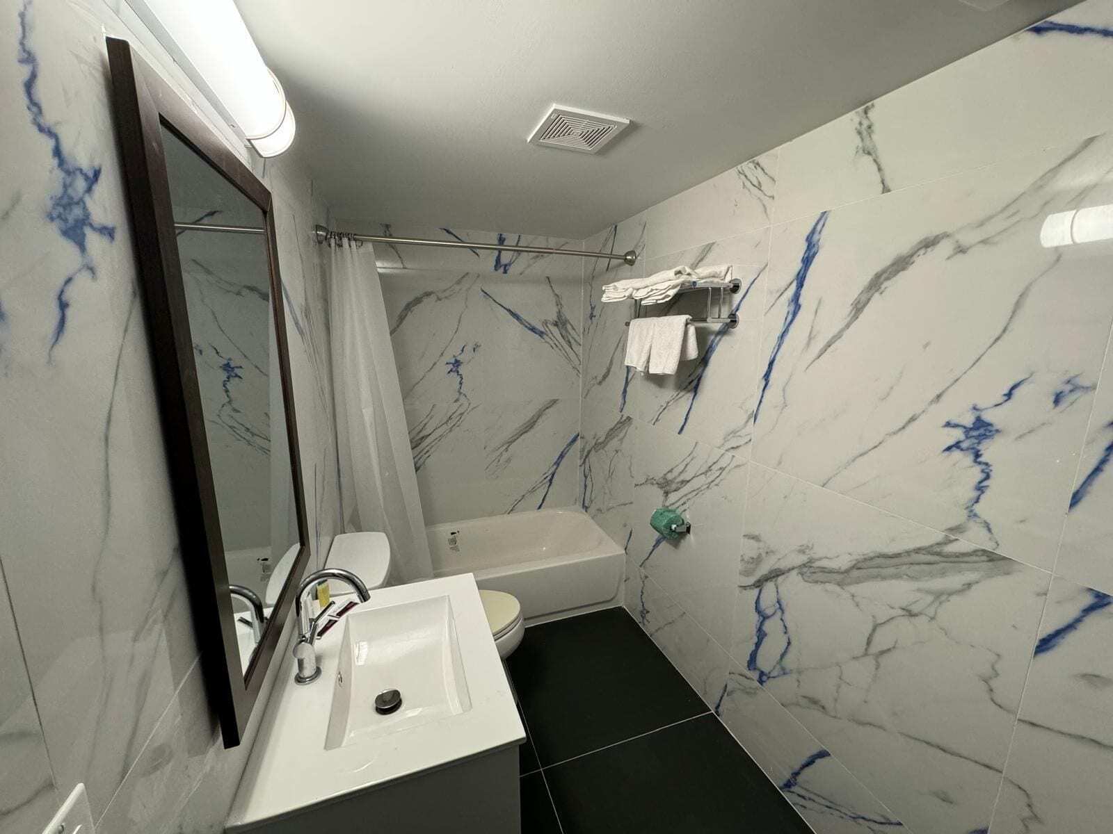 A modern bathroom with a white sink, black floor tiles, and marble walls.
