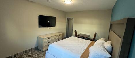 A hotel room with a bed, a dresser, a television, and a small table with chairs.
