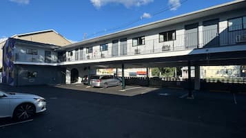 Un motel de dos pisos con una zona de estacionamiento techada y un edificio de un solo piso contiguo.