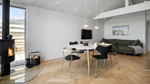 Ein modernes Wohnzimmer mit Kamin, einem Essbereich mit rundem Tisch und Stühlen, einer Couch und einem an der Wand befestigten Fernseher.