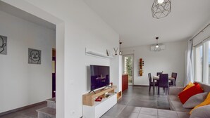 A modern living room with a flat-screen TV, a dining area with a table and chairs, and a sofa with colorful cushions. - Splendida casa in Corsanico (Massarosa)