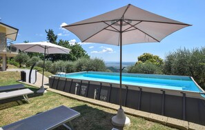 Une piscine extérieure avec deux parasols, une chaise longue et une vue sur le paysage.