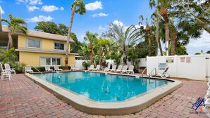 A swimming pool with lounge chairs and palm trees. - Waves 4, poolside condo, 5 min walk to beach and entertainment (St. Pete Beach)