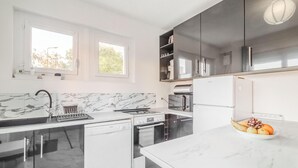 Une cuisine moderne avec un dosseret en marbre, des appareils en acier inoxydable et un panier de fruits posé sur le plan de travail.