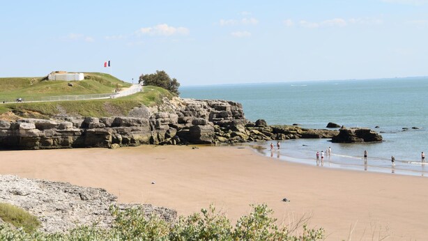 Une plage bordée de falaises rocheuses, un drapeau et un ciel dégagé.