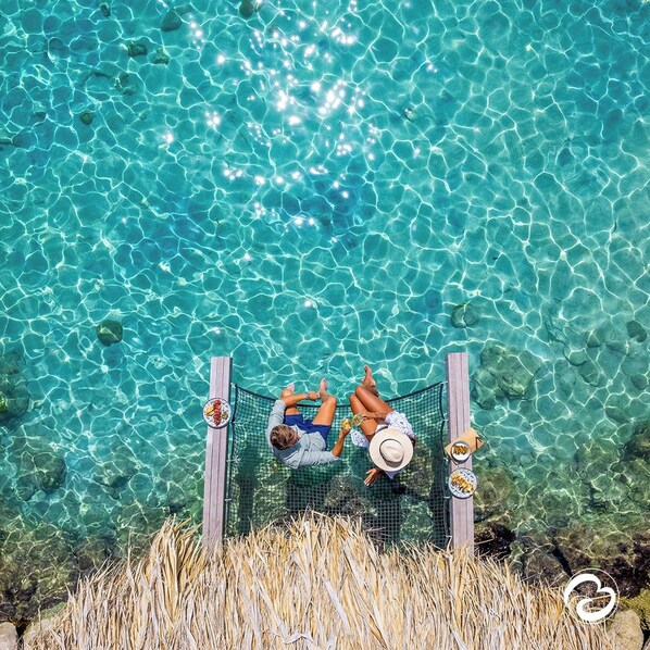 A hammock over a pool with clear water, surrounded by dry grass.