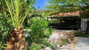 Une maison de campagne rustique, dotée d’un porche abrité, entourée d’une végétation luxuriante et sous un ciel dégagé.