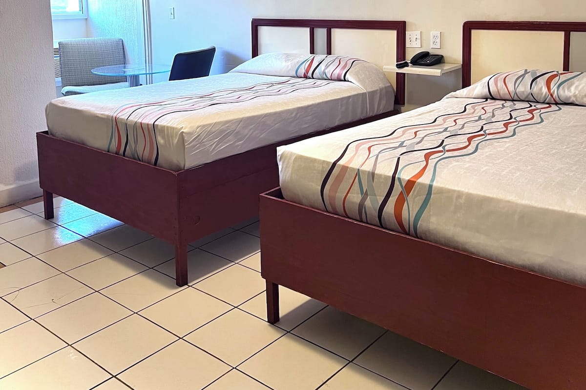 A hotel room with two beds, a ceiling fan, a window, and a small table.