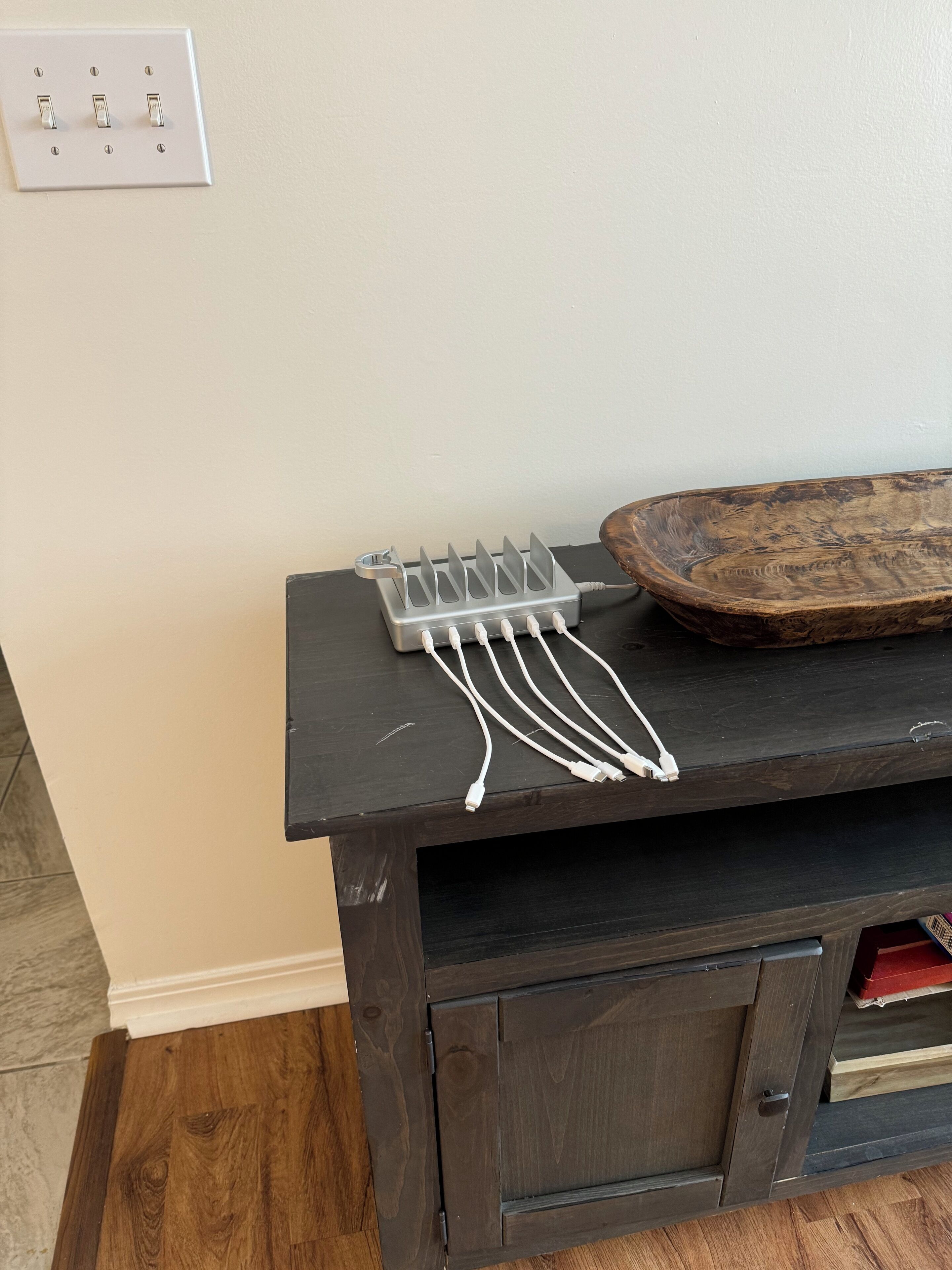 A wooden cabinet with a dark finish, a power strip, and a wooden bowl on top.