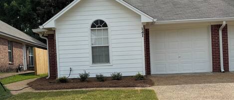 A single-story house with a garage, a front yard with grass and a small garden, and a brick foundation.