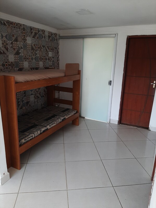 A room with a bunk bed, a patterned wall, a tiled floor, and a door. - Chácara do Allan (Manhuaçu)