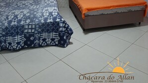 Ein Zimmer mit zwei Betten, eines mit einem gemusterten Überwurf und das andere mit einer orangefarbenen Decke. Das Zimmer hat einen Wandteppich mit Muster und einen Fliesenboden.