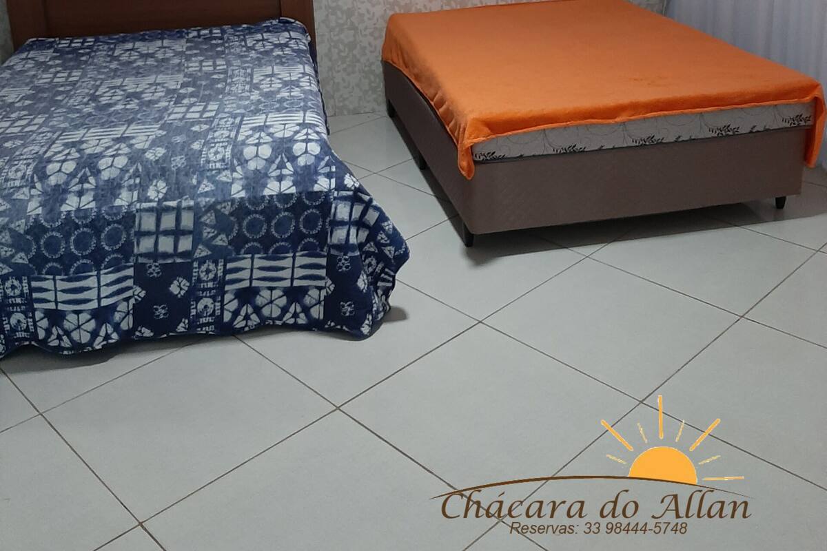Une chambre avec deux lits, l’un recouvert d’une couvre-lit à motifs et l’autre d’une housse orange. La chambre est dotée d’un papier peint à motifs et d’un sol carrelé.
