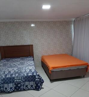 A room with two beds, one with a patterned bedspread and the other with an orange cover. The room has patterned wallpaper and a tiled floor. - Chácara do Allan (Manhuaçu)