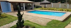 A rectangular swimming pool with a tiled deck, surrounded by well-maintained grass and a stone border. - Chácara do Allan (Manhuaçu)