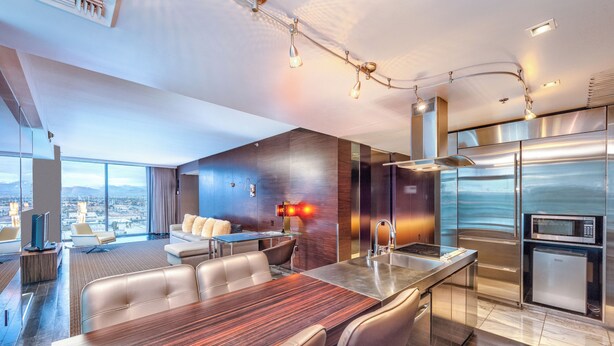 Una habitación de hotel moderna con zona de comedor, un amplio ventanal con vistas a la ciudad, televisor de pantalla plana y minibar.