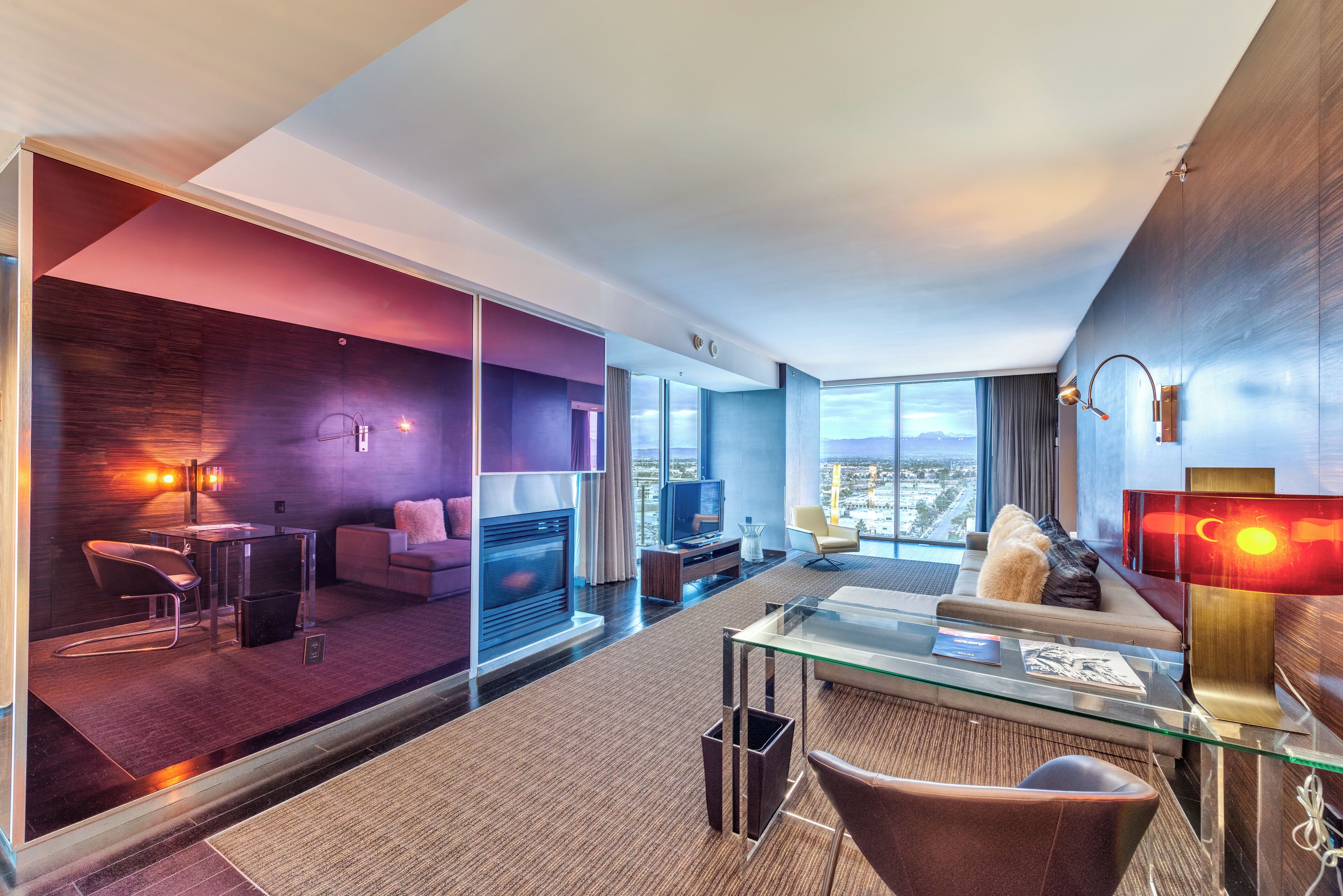 Una habitación de hotel moderna con un separador de vidrio, un sofá, una mesa de centro, un televisor y vistas a la ciudad.
