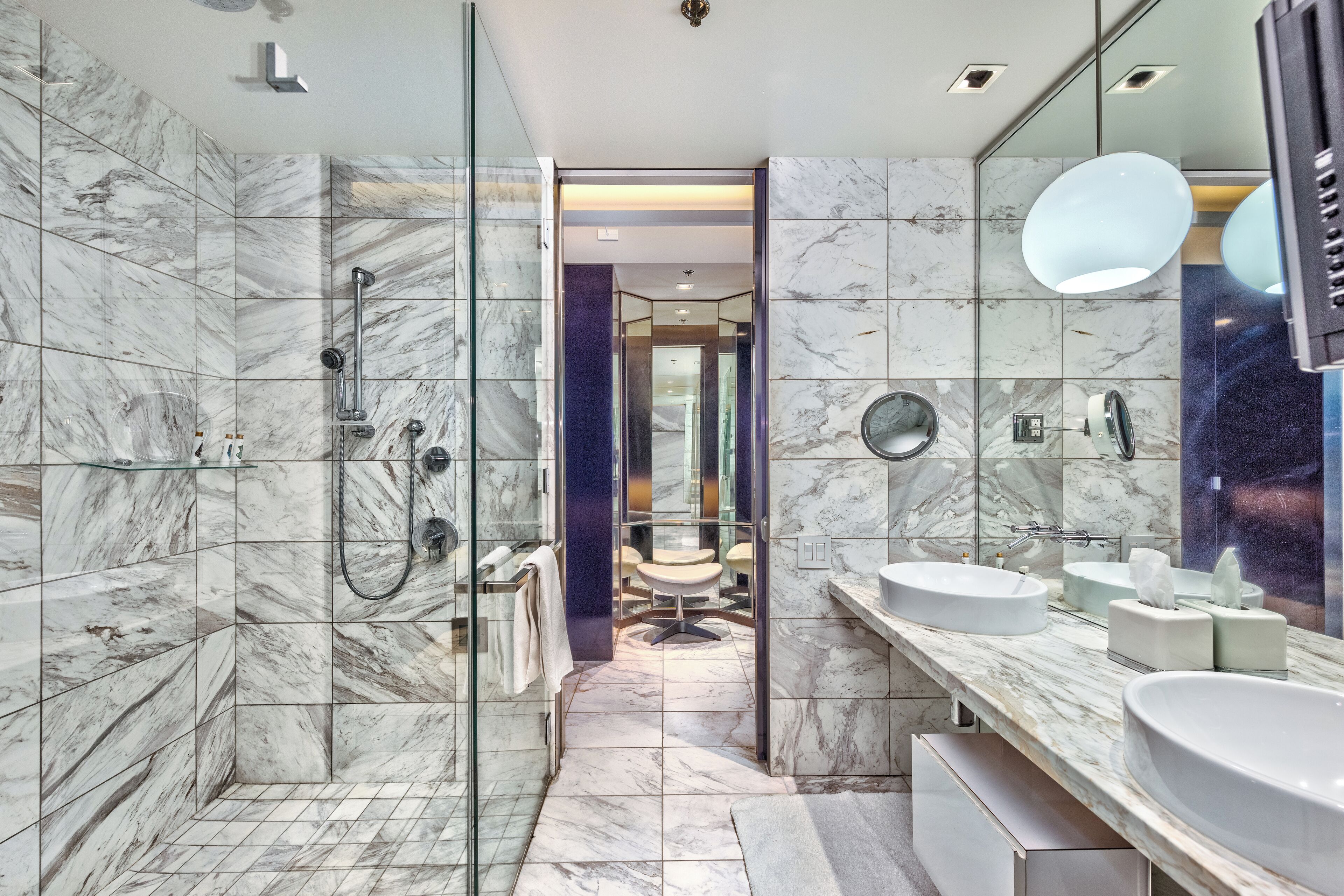 Un bagno moderno con piastrelle in marmo, box doccia in vetro e lavabo doppio.