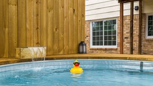 Uma piscina com um pato de borracha usando óculos de sol, um deck de madeira e um muro de tijolos.