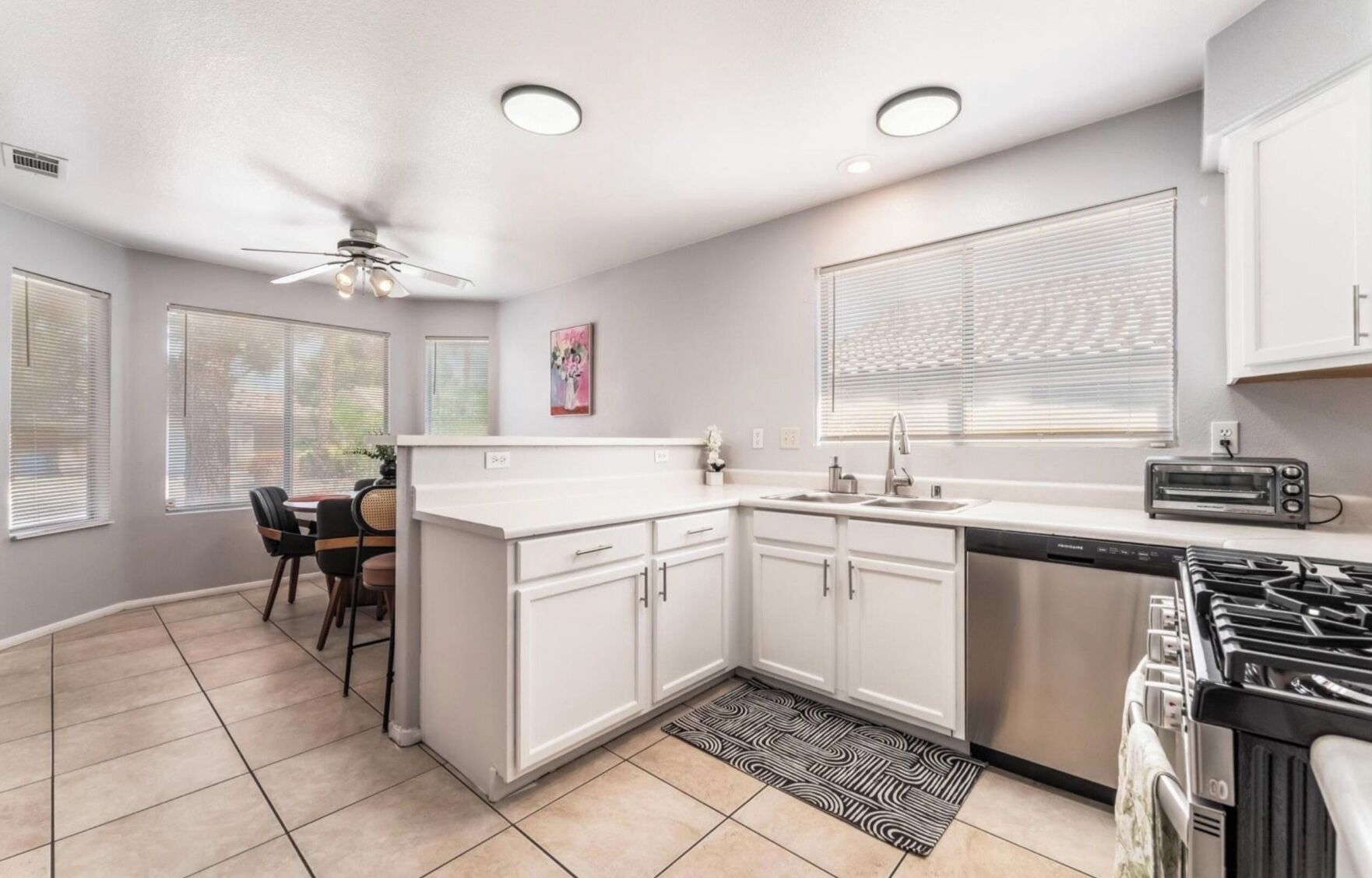 A modern kitchen with white cabinets, a black stove, and a dining area with a table and chairs.