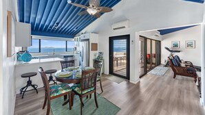 A modern kitchen with a view of the sea, a dining area with a table and chairs, and a living area with a sofa and a treadmill. - Generator! Top Floor Condo - 5 mins to Magens (St. Thomas)