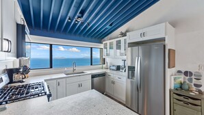 A modern kitchen with a view of the ocean, stainless steel appliances, and white cabinetry. - Generator! Top Floor Condo - 5 mins to Magens (St. Thomas)