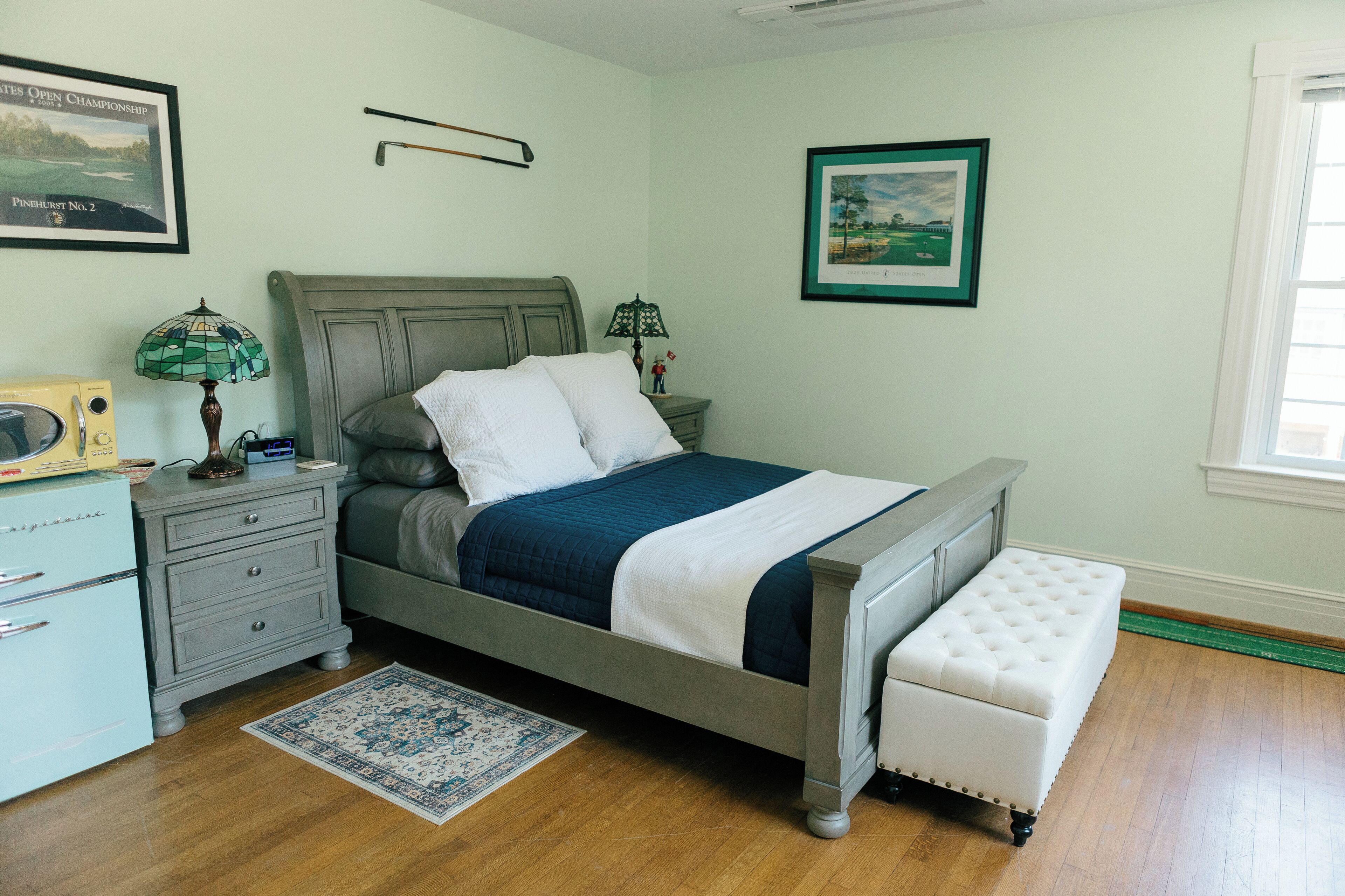 A bedroom with a bed, bedside tables, a nightstand, a dresser, a lamp, a rug, and framed pictures on the walls.