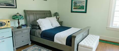 A bedroom with a bed, bedside tables, a nightstand, a dresser, a lamp, a rug, and framed pictures on the walls.