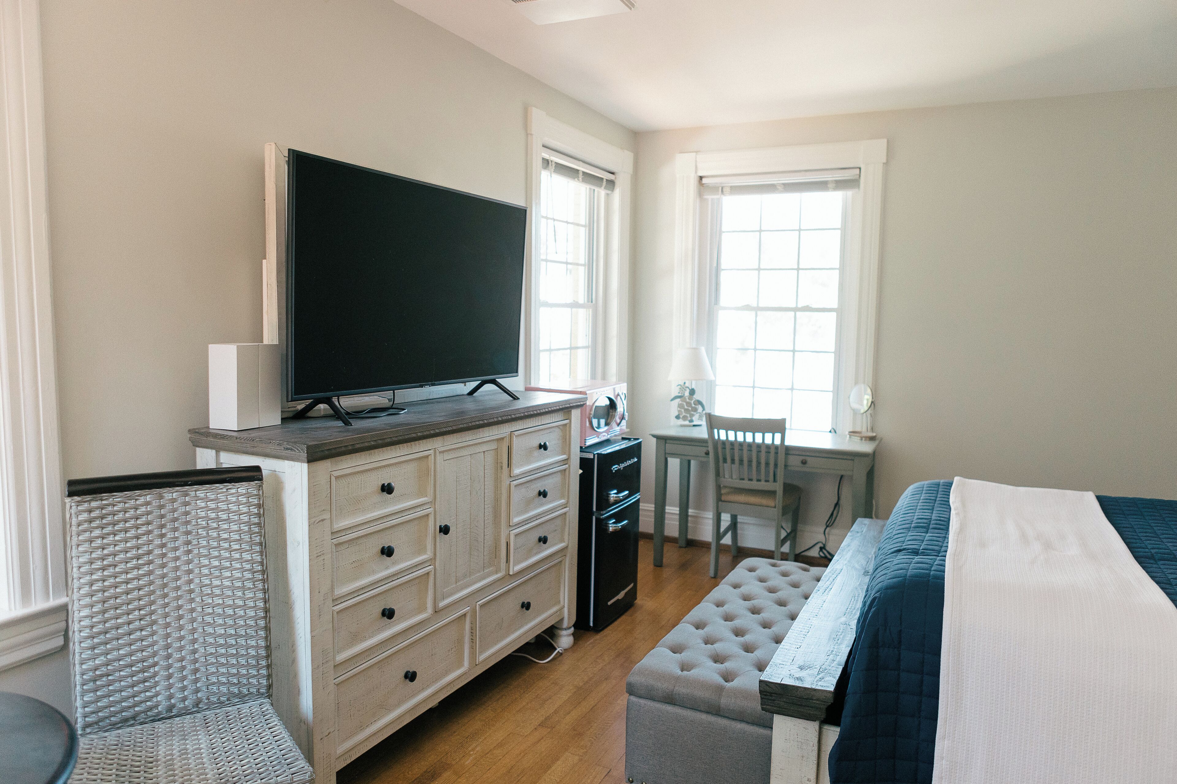 A bedroom with a bed, a dresser, a television, a desk, and a chair.