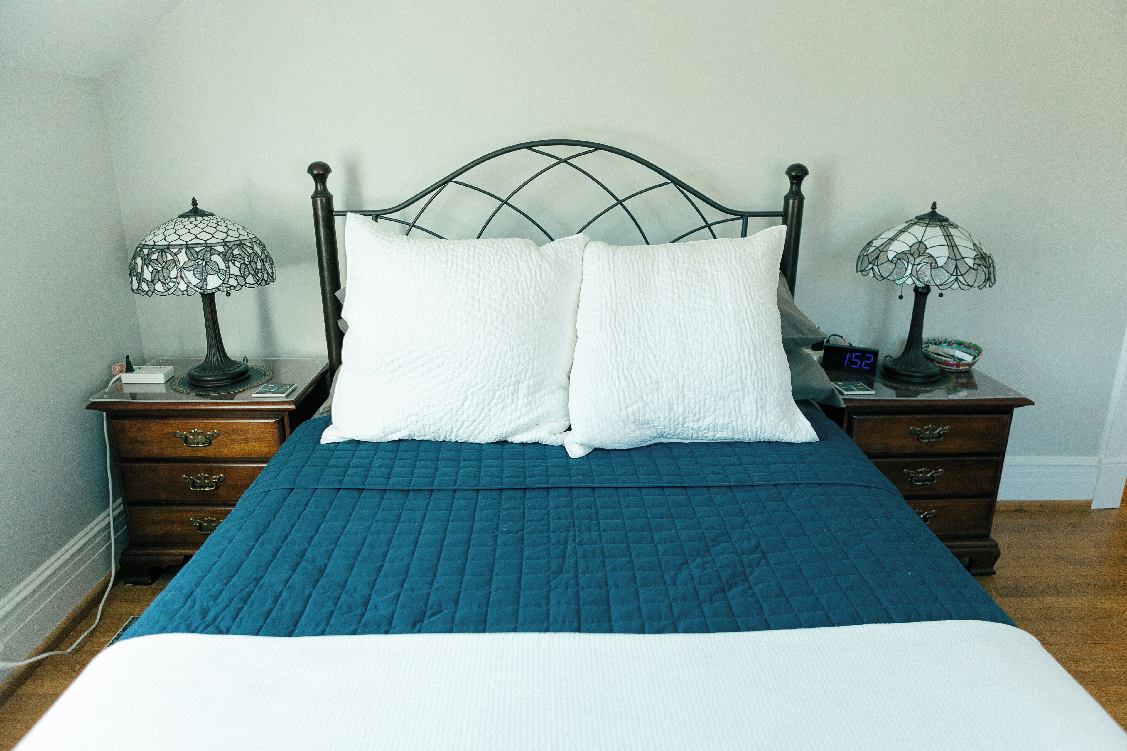 A neatly made bed with a blue quilt, two white pillows, and two table lamps on nightstands.