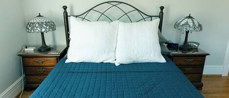 A neatly made bed with a blue quilt, two white pillows, and two table lamps on nightstands.