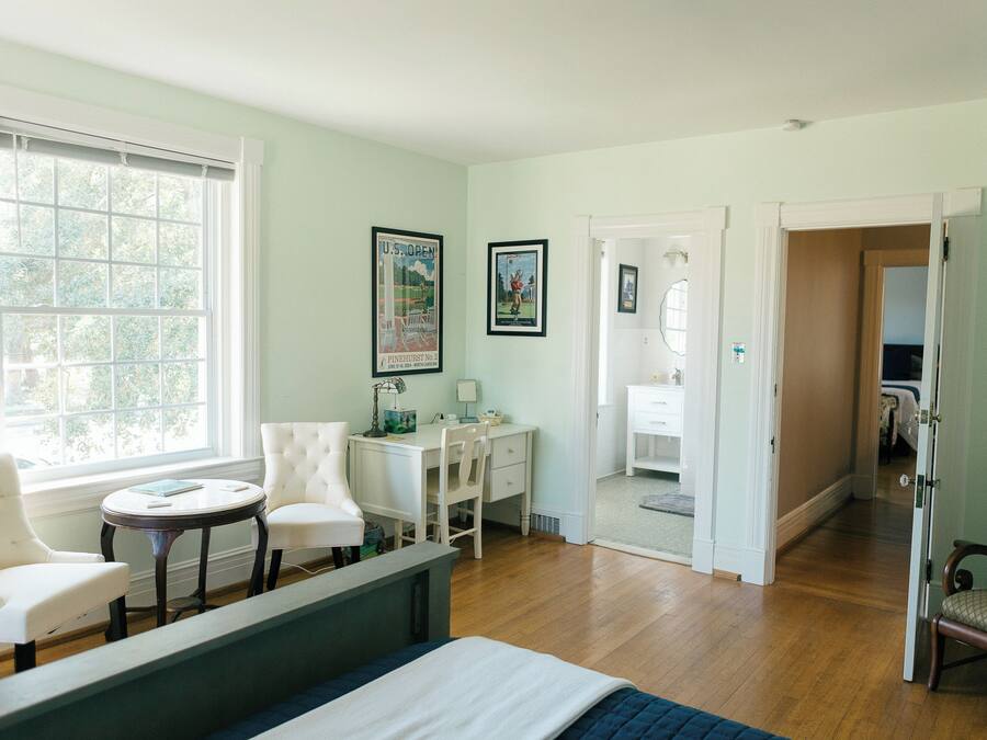 A bedroom with a bed, two chairs, a desk, and a window.