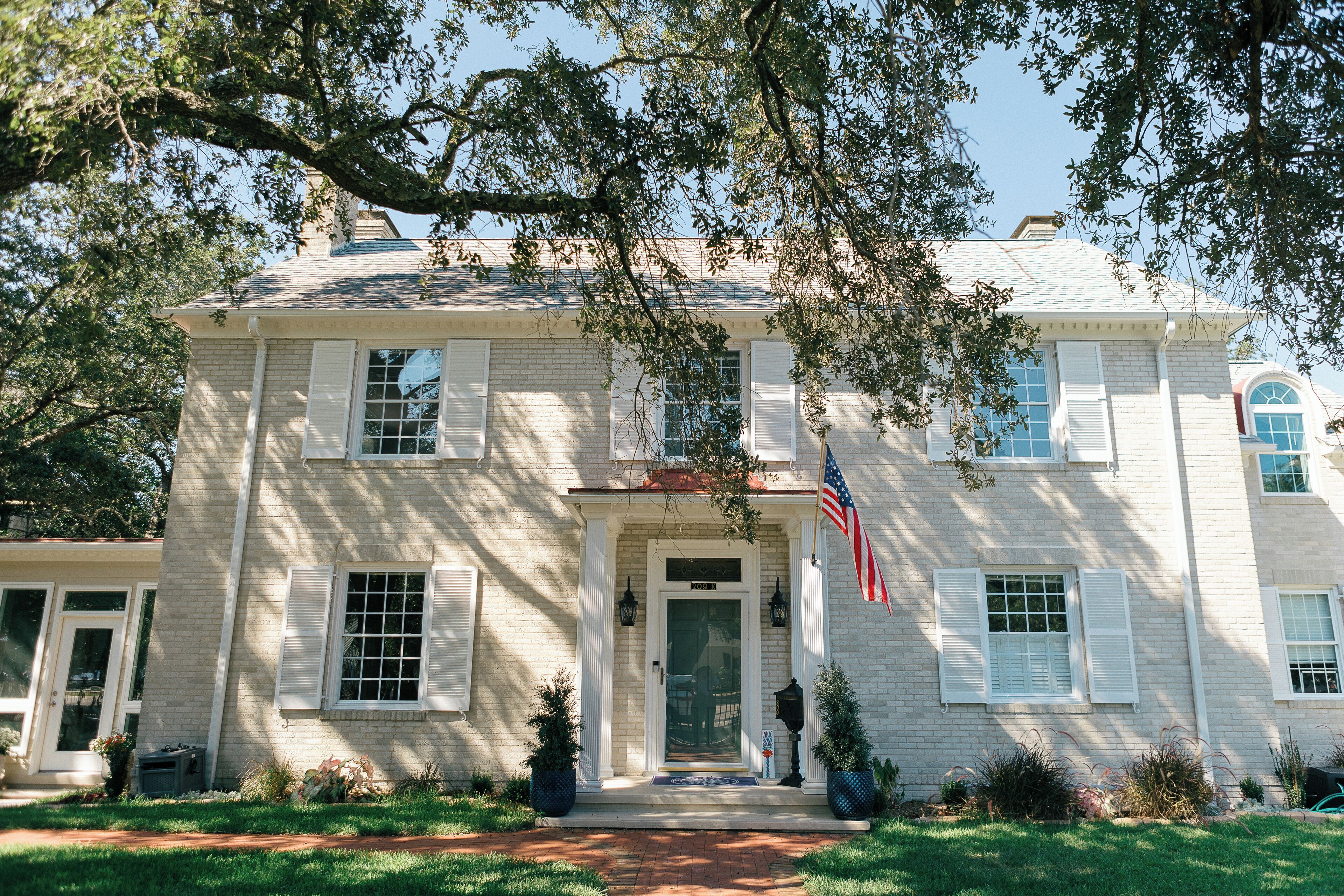 A two-story house with a front porch, a brick facade, and a flag.