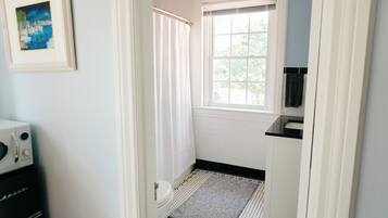A narrow bathroom with a window, a shower curtain, a toilet, and a small sink area.