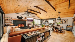 A spacious living area with a fireplace, leather sofa, wooden flooring, and a dining area with a table and chairs.