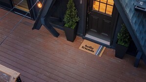 A modern house with a steeply pitched roof, a dark entrance, and a welcome mat that reads "hello friends".