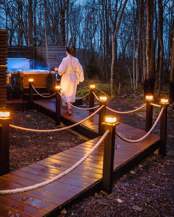 Un sentier en bois mène à un bâtiment doté d’un espace spa, le tout étant entouré d’arbres.
