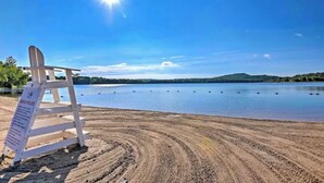 A beach with a wooden chair and a signboard, surrounded by calm water and distant hills.