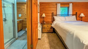 A wooden cabin bedroom with a bed, two bedside lamps, a nightstand, and a window with curtains.
