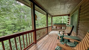 A wooden porch with benches and a view of a forest.