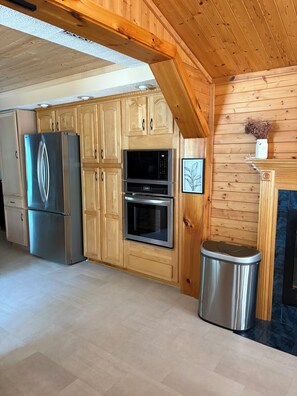 Eine Küche mit Holzschränken, einem Edelstahlkühlschrank, einer Mikrowelle, einem Backofen und einem Mülleimer.