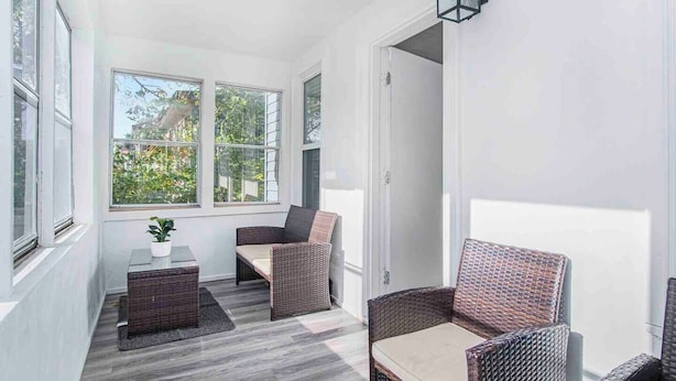 A sunroom with large windows, wicker furniture, and a small table with a plant. - Monthly Stays at Brightside Bungalow: Near Downtown Muskegon (Muskegon)