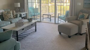 En rummelig stue med en stor skydedør, der fører ud til en balkon. Der er ventilator i loftet, et sofabord og to sofaer.
