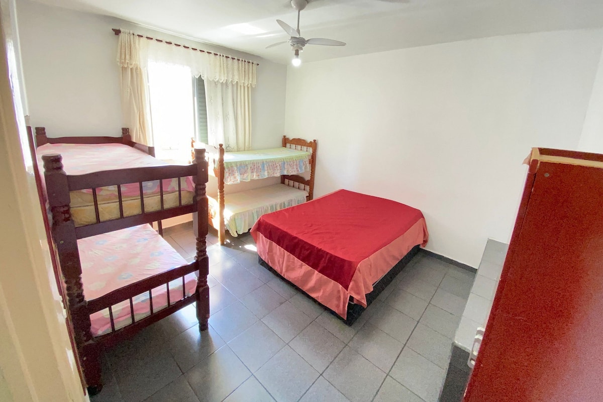 Un dormitorio con dos literas y una cama individual, un ventilador de techo y una ventana con cortinas.