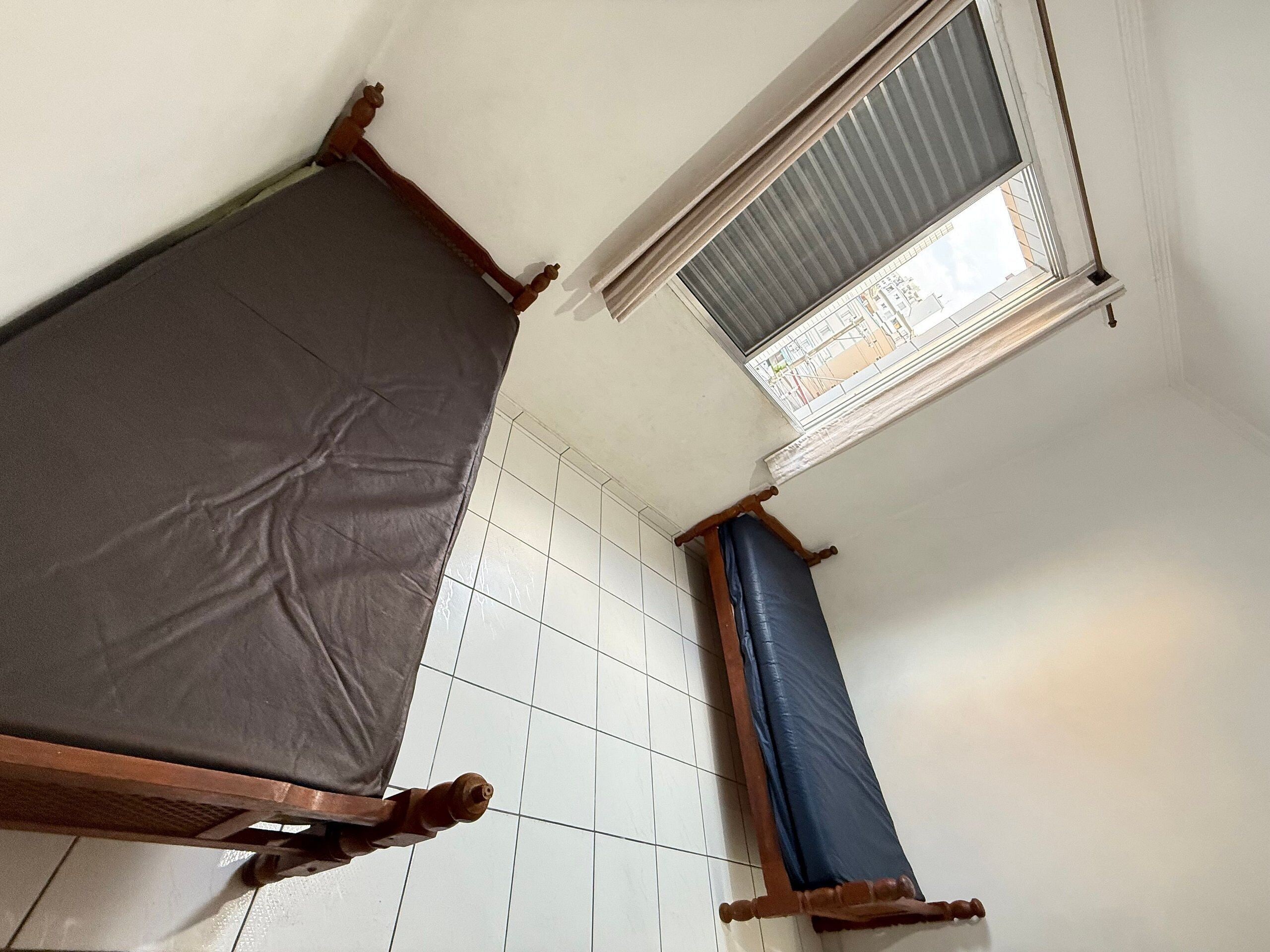 Una habitación con dos camas, una ventana con persianas y piso de baldosas.