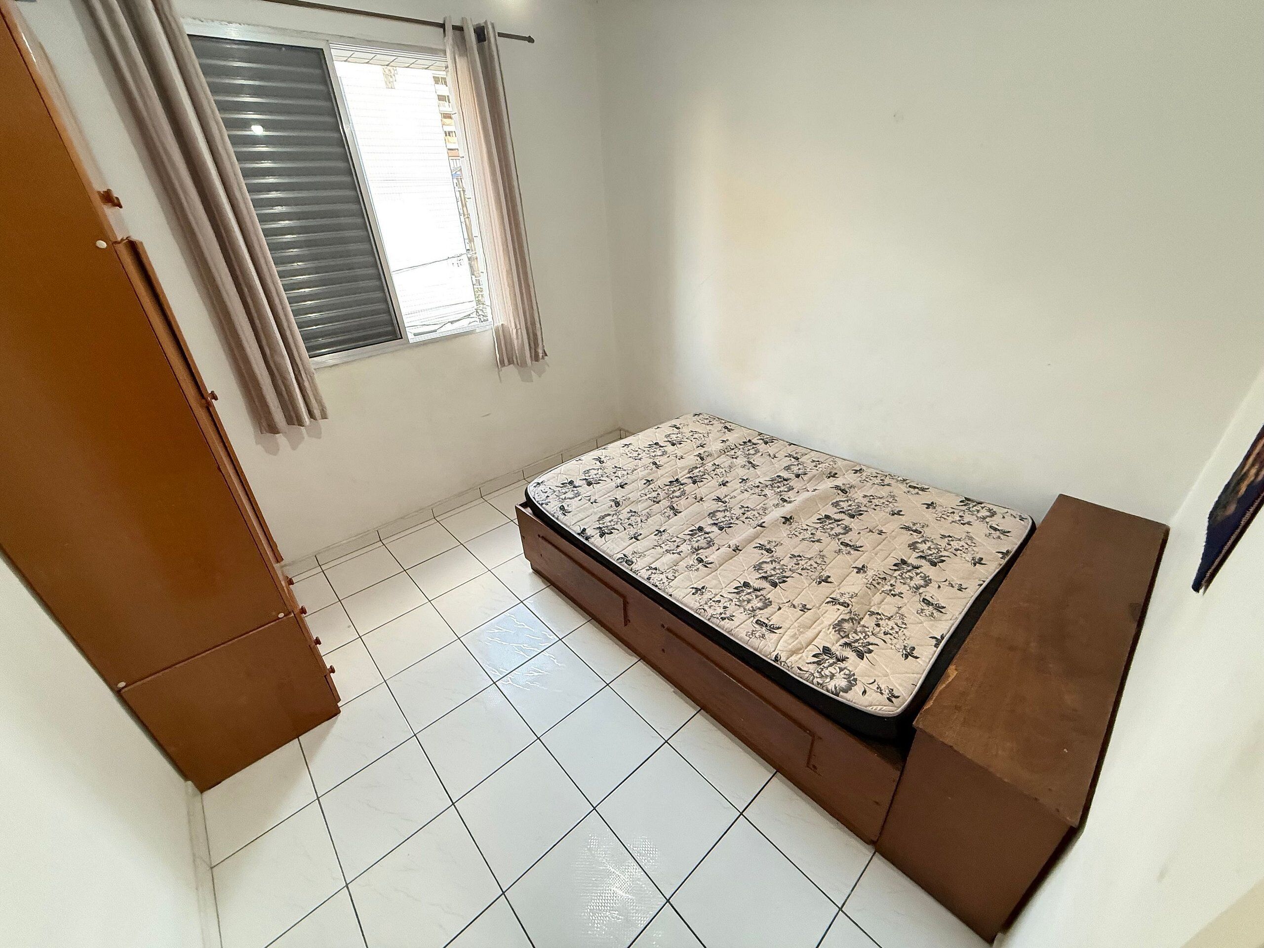 A bedroom with a bed, a window with curtains, and a tiled floor.