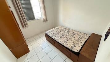 A bedroom with a bed, a window with curtains, and a tiled floor.